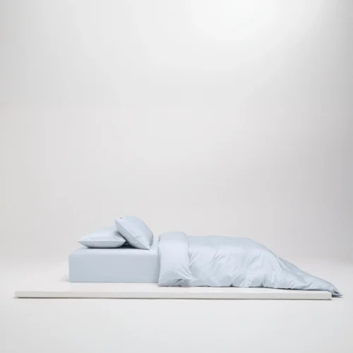 Uppbäddad säng i Shade Ice Blue satin, tillverkad av 100 % ekologisk bomull och GOTS-certifierad.